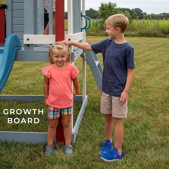 Backyard Discovery Beacon Heights Elevated Cedar Wooden Kids Playhouse with Wave Slide, Play Kitchen, Wrap-Around Deck, Flat-Step Ladder, Half Door, Windows, Bell, and Growth Chart for Outdoor Play